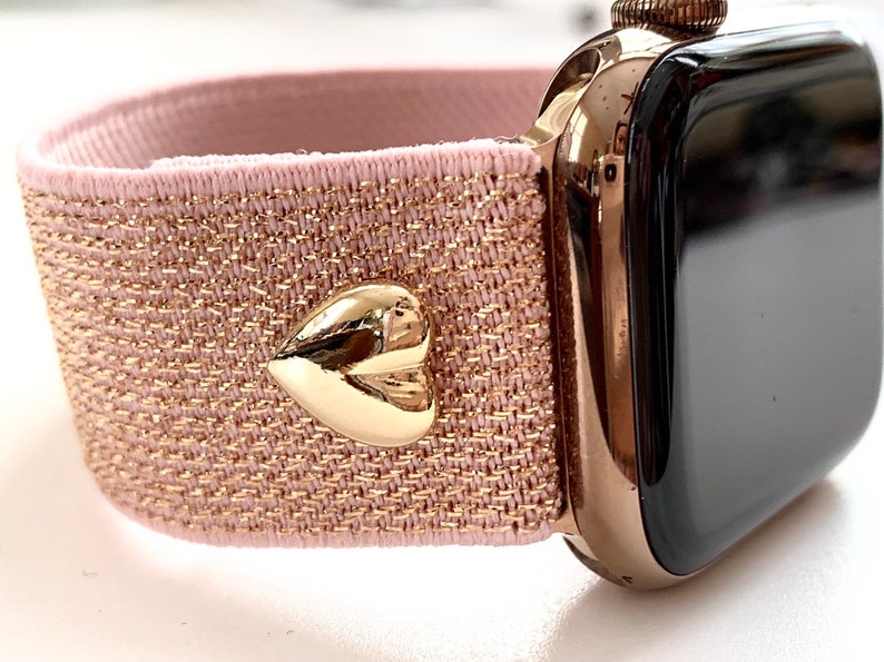 May include: A rose gold Apple Watch with a pink and gold glitter elastic band and a gold heart charm.