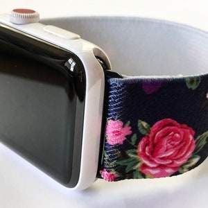 May include: A white Apple Watch with a black face and a navy blue and floral patterned elastic band.