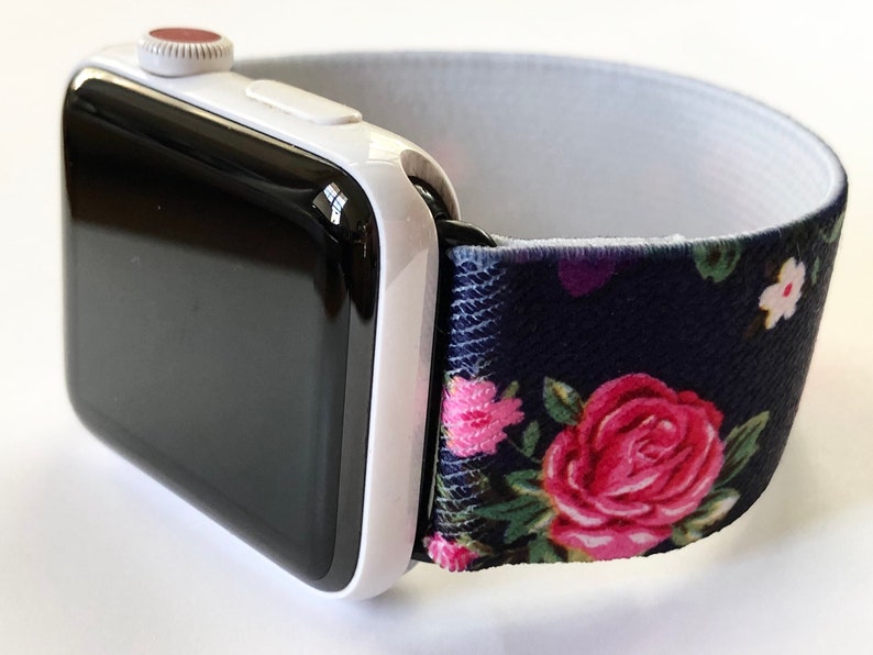 May include: A white Apple Watch with a black face and a navy blue and floral patterned elastic band.