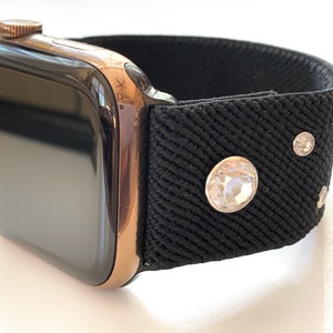 May include: A black Apple Watch with a rose gold band and a black fabric band with rhinestones.