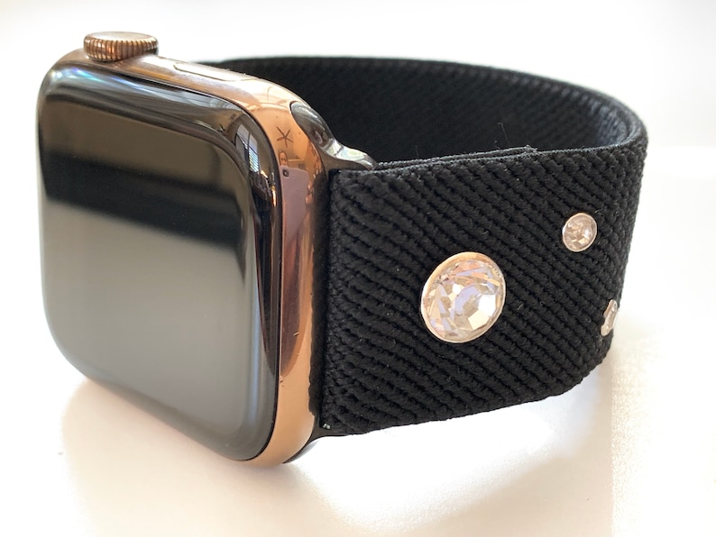 May include: A black Apple Watch with a rose gold band and a black fabric band with rhinestones.
