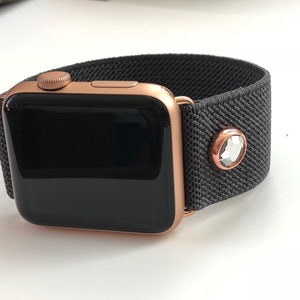 May include: A rose gold Apple Watch with a black elastic band and a clear crystal accent.