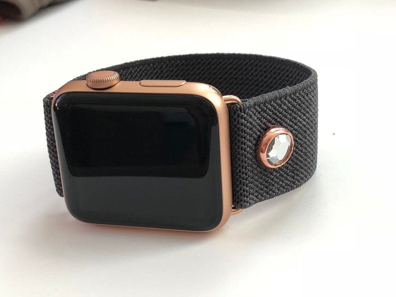 May include: A rose gold Apple Watch with a black elastic band and a clear crystal accent.