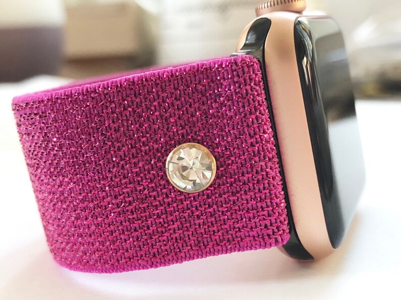 May include: A pink glitter watch band with a clear rhinestone accent. The band is compatible with Apple Watch.