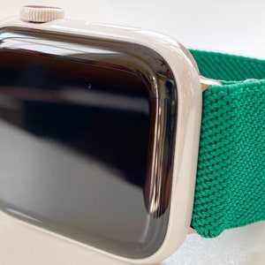 K&ouml;nnte beinhalten: Eine silberne Apple Watch mit einem gr&uuml;nen Sportarmband. Das Zifferblatt der Uhr ist schwarz und das Armband besteht aus einem weichen, dehnbaren Material.