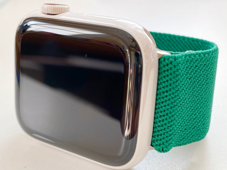 K&ouml;nnte beinhalten: Eine silberne Apple Watch mit einem gr&uuml;nen Sportarmband. Das Zifferblatt der Uhr ist schwarz und das Armband besteht aus einem weichen, dehnbaren Material.