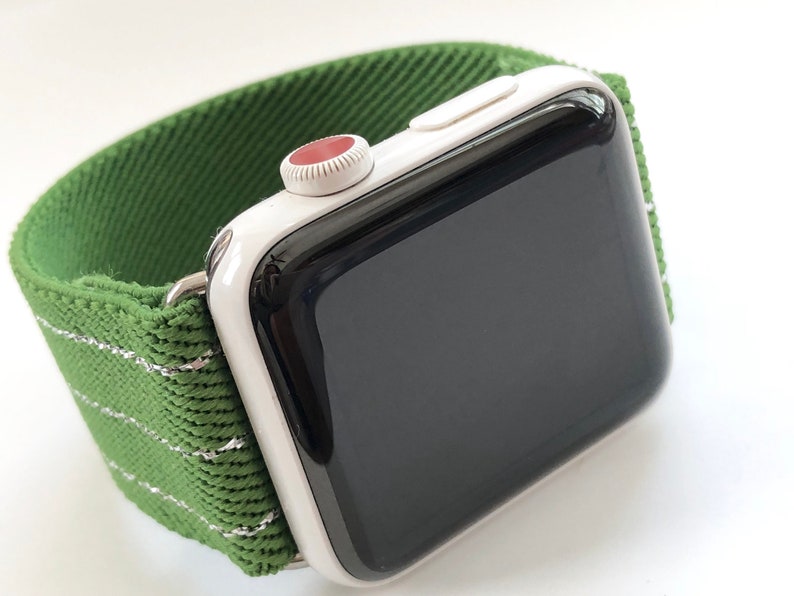 Puede incluir: Un Apple Watch blanco con una esfera negra y una banda deportiva verde. La banda tiene una franja blanca que recorre el centro.