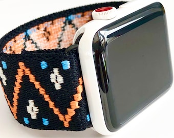 May include: A black and white patterned watch band with orange and blue accents. The band is attached to a white Apple Watch with a black face.