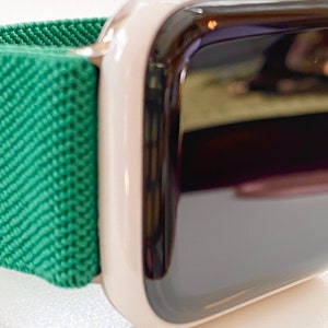 K&ouml;nnte beinhalten: Eine wei&szlig;e Apple Watch mit einem gr&uuml;nen Sportarmband. Das Zifferblatt der Uhr ist schwarz und reflektierend.