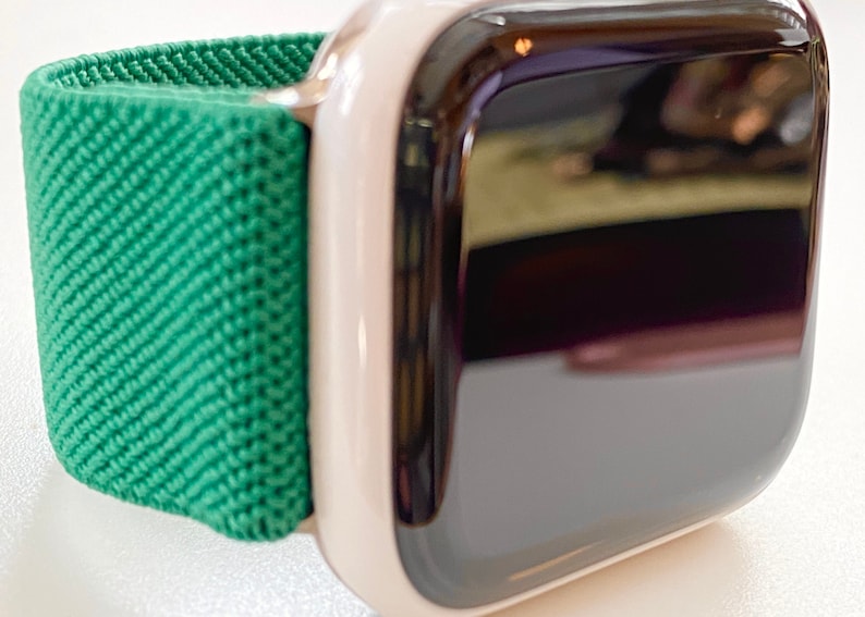 K&ouml;nnte beinhalten: Eine wei&szlig;e Apple Watch mit einem gr&uuml;nen Sportarmband. Das Zifferblatt der Uhr ist schwarz und reflektierend.