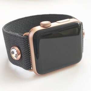 May include: A rose gold Apple Watch with a black sport band and clear crystal accents.