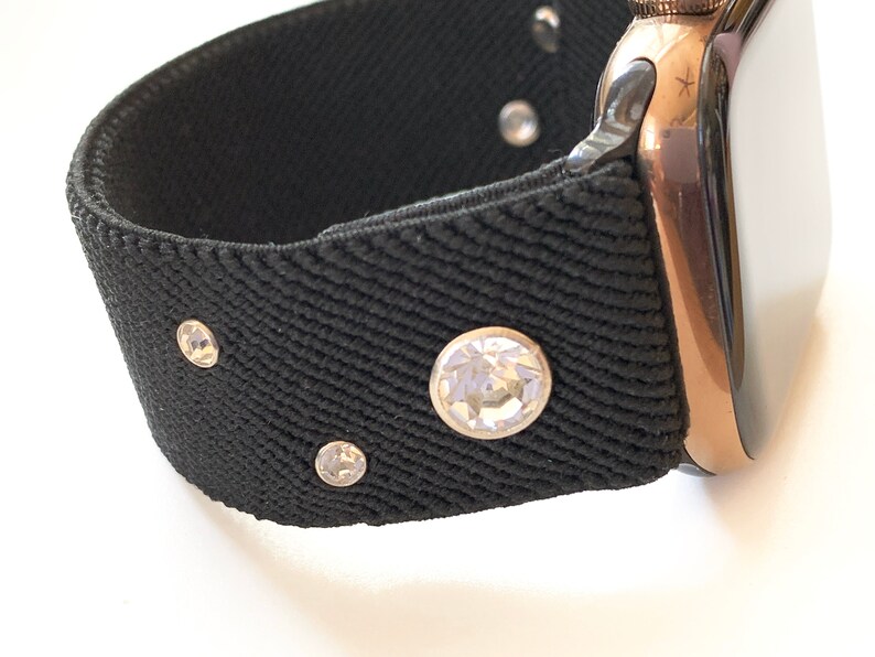 May include: A black watch band with rhinestones. The band is made of a stretchy material and has a rose gold watch face.