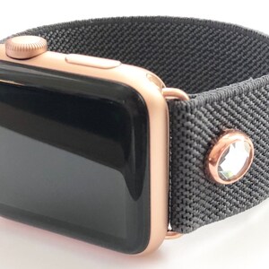 May include: A rose gold Apple Watch with a black face and a gray elastic band with a single rhinestone accent.