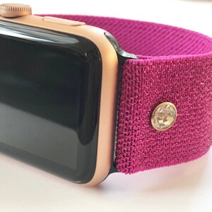May include: A rose gold Apple Watch with a pink fabric band and a clear rhinestone accent.
