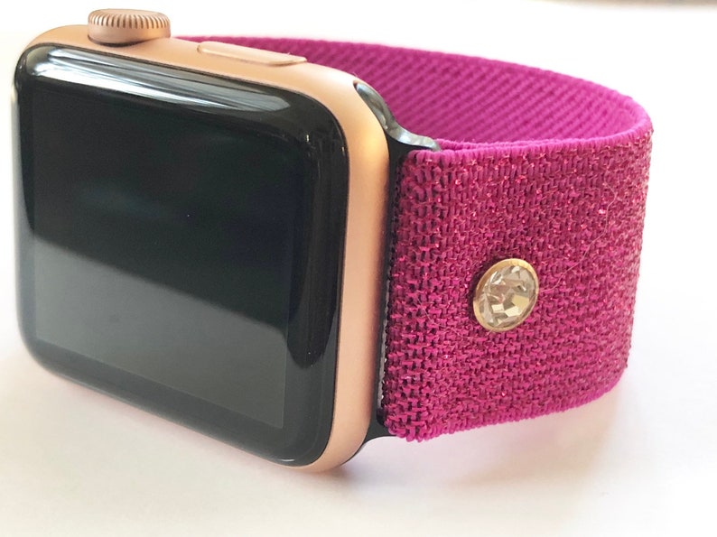 May include: A rose gold Apple Watch with a pink fabric band and a clear rhinestone accent.