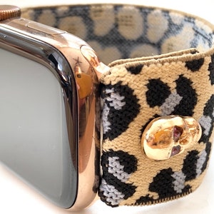 Puede incluir: Un Apple Watch de oro rosa con una banda de reloj de estampado de leopardo y una hebilla con forma de calavera.