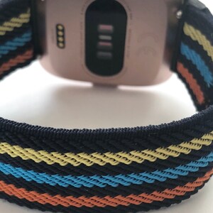 May include: A rose gold smartwatch with a black and multi-colored striped band. The band has yellow, blue, and orange stripes.