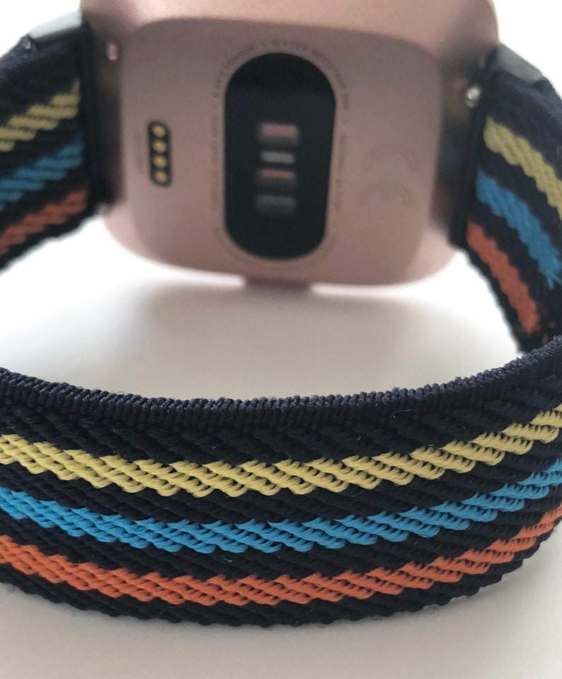 May include: A rose gold smartwatch with a black and multi-colored striped band. The band has yellow, blue, and orange stripes.