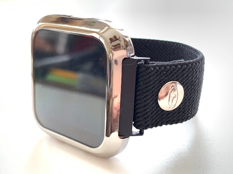 May include: A silver smartwatch with a black fabric band. The band has a silver buckle and a silver button with a logo.
