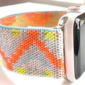 May include: A colorful knitted watch band in shades of orange, yellow, blue, and white. The band is attached to a white Apple Watch.