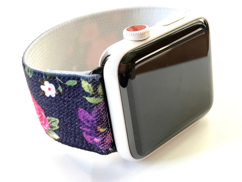 May include: A white Apple Watch with a black face and a floral patterned elastic band. The band is navy blue with pink, purple, and green flowers.