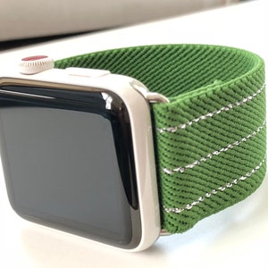 Puede incluir: Un Apple Watch plateado con una banda de tela verde. La banda tiene un detalle de costura blanca.