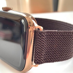 Puede incluir: Un Apple Watch de oro rosa con una banda deportiva de bucle de color marr&oacute;n oscuro.