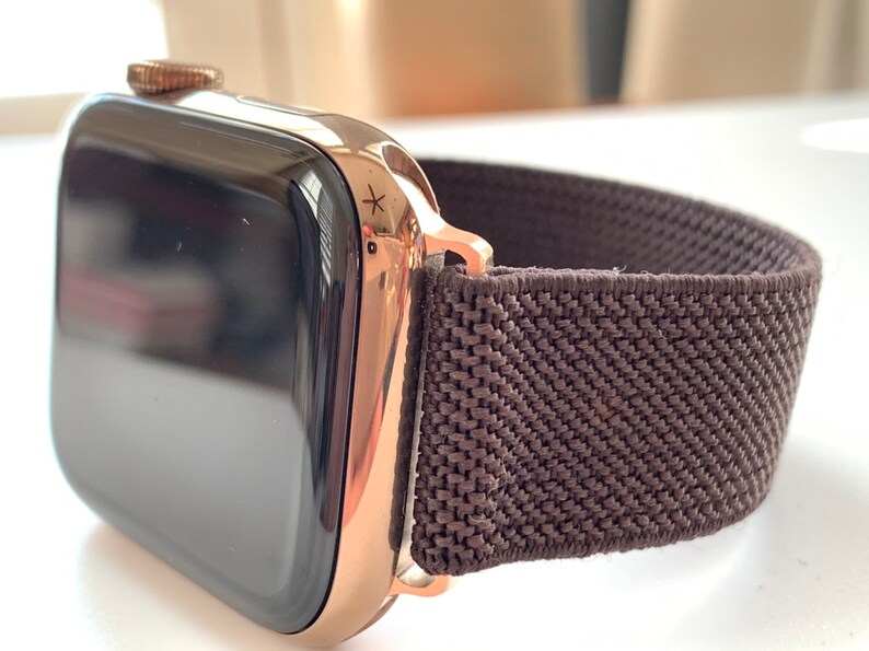 Puede incluir: Un Apple Watch de oro rosa con una banda deportiva de bucle de color marr&oacute;n oscuro.