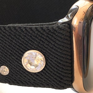May include: A black watch band with three clear rhinestones. The band is attached to a rose gold Apple Watch.