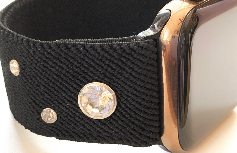 May include: A black watch band with three clear rhinestones. The band is attached to a rose gold Apple Watch.