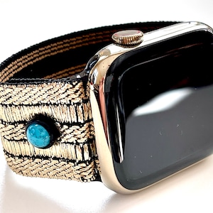 May include: A gold and black woven watch band with turquoise accents. The band is attached to a black Apple Watch with a silver case.
