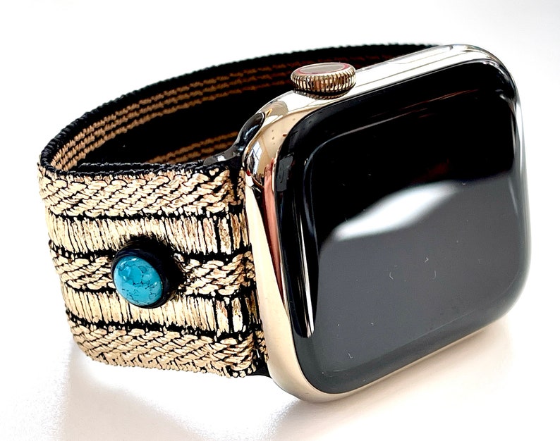 May include: A gold and black woven watch band with turquoise accents. The band is attached to a black Apple Watch with a silver case.