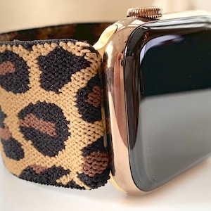 Puede incluir: Un Apple Watch dorado con una pantalla negra y una banda elástica de estampado de leopardo.