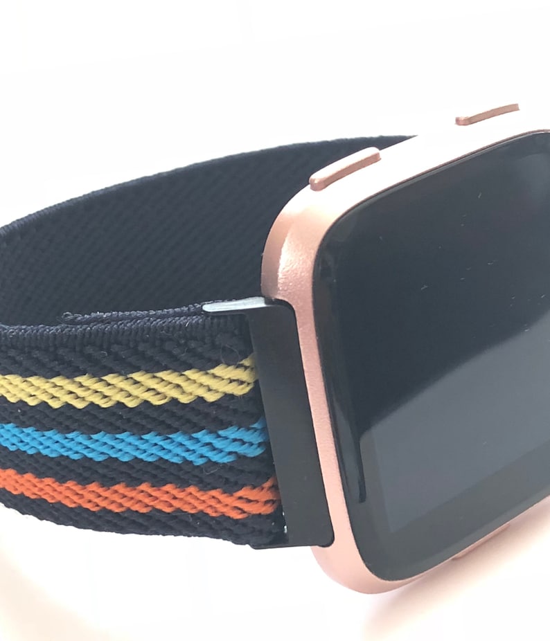 May include: A rose gold smartwatch with a black and multi-colored striped elastic band.
