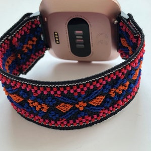 May include: A rose gold smartwatch with a black and colorful patterned band. The band has a geometric design with red, orange, blue, and pink accents.