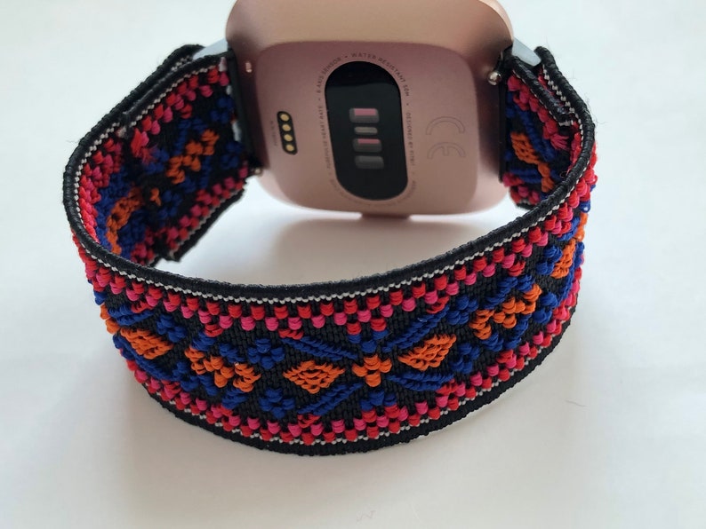 May include: A rose gold smartwatch with a black and colorful patterned band. The band has a geometric design with red, orange, blue, and pink accents.