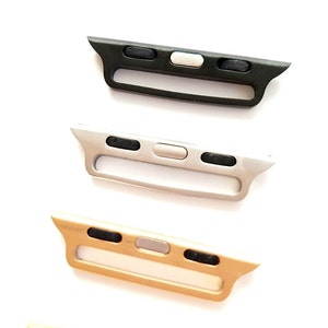 May include: Three Apple Watch band adapters in black, silver, and gold. Each adapter has a slot for a watch band and three buttons.