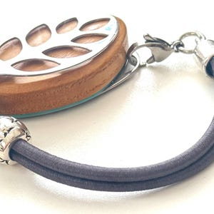 May include: A wooden and silver fitness tracker with a leaf design, attached to a dark gray elastic bracelet.
