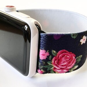 May include: A white Apple Watch with a black face and a navy blue and floral patterned elastic band.