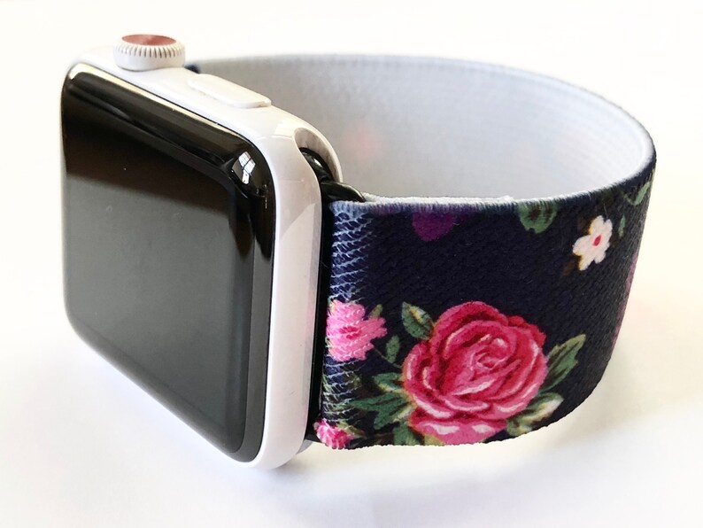 May include: A white Apple Watch with a black face and a navy blue and floral patterned elastic band.