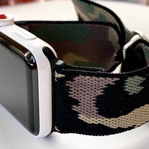 May include: A white Apple Watch with a black and green camouflage elastic band.