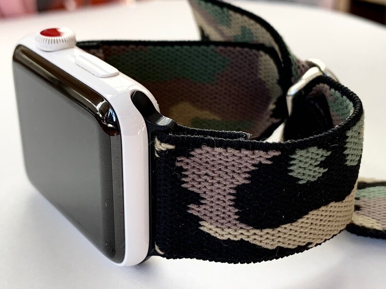 May include: A white Apple Watch with a black and green camouflage elastic band.