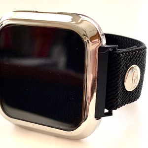 May include: A silver watch case with a black screen and a black elastic band. The band has a silver buckle with a logo.