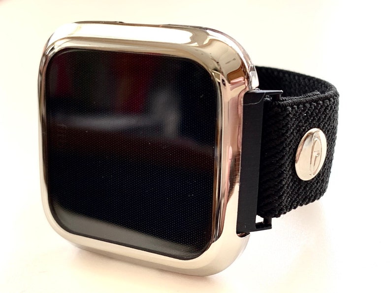 May include: A silver watch case with a black screen and a black elastic band. The band has a silver buckle with a logo.