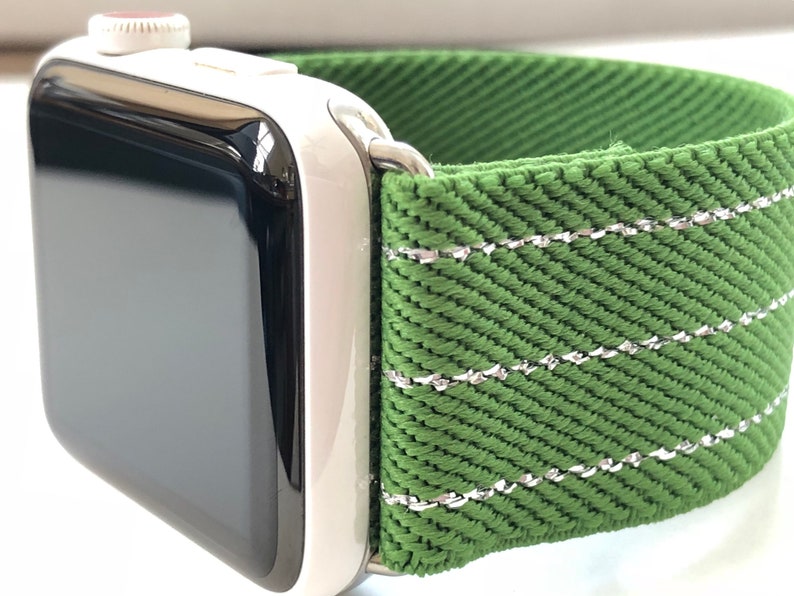 Puede incluir: Una banda de reloj Apple verde con costuras plateadas. La banda est&aacute; hecha de una tela tejida.