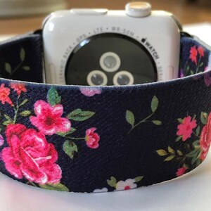 May include: A navy blue watch strap with a floral print featuring pink and purple flowers. The strap is made of a soft, textured material and is compatible with Apple Watch.
