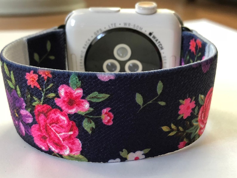 May include: A navy blue watch strap with a floral print featuring pink and purple flowers. The strap is made of a soft, textured material and is compatible with Apple Watch.