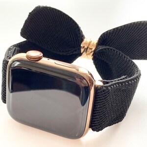 May include: A gold Apple Watch with a black woven band and a black fabric bow.