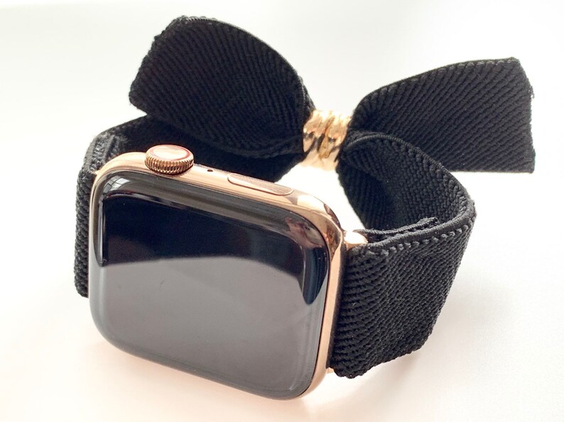 May include: A gold Apple Watch with a black woven band and a black fabric bow.