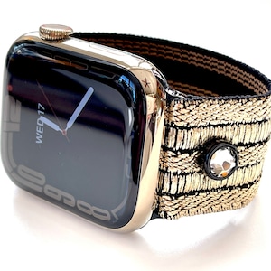 May include: A gold Apple Watch with a black and gold patterned band. The watch face displays the date and time, showing "WED 17".